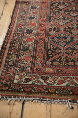 Distressed Kurdish rug corner, rust red floral borders, diamond lattice field, and fringe.