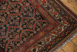 Distressed Kurdish rug corner with rust red floral border, diamond lattice, and fringe.
