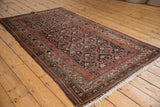 Distressed Kurdish rug corner detail with light fringe, brick red border, and worn pile.