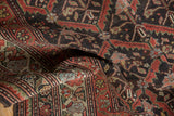 Folded distressed Kurdish rug, showcasing charcoal, rust, and green floral star patterns.