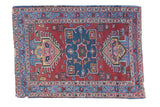Playful distressed Heriz rug with a blue medallion on a brick red field and colorful geometric borders.