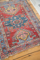 Angled corner of a vintage Heriz rug showing its tattered end and colorful geometric border.
