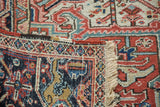 Hand-knotted Heriz carpet's folded edge reveals intricate geometric motifs, rich indigo, brick red, and fringe.