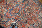 Feet on vintage Heriz carpet with geometric patterns, brick red, blue, and even wear.