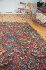 Brick red field of a vintage Heriz rug with exaggerated leaf designs in blue, green, blush.