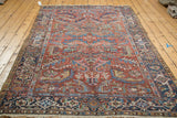 Vintage Heriz rug with navy geometric border and stylized brick red, blue, and blush patterns.