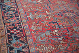Vintage Heriz carpet close-up, featuring brick red, navy, and teal geometric and curvilinear patterns.