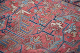 Detail of vintage Heriz rug, brick red ground with blue geometric sickle leaf patterns.