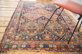 Distressed Afshar rug displaying tribal serrated panels, floral motifs, and terra cotta, navy colors.