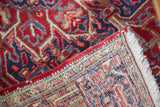 Folded Vintage Northwest Persian rug displaying hand-knotted foundation, cherry red and navy geometric pile, fringe.