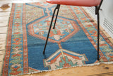 Distressed antique Northwest Persian rug corner, highlighting geometric patterns in indigo, rust, and pale green.
