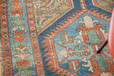 Distressed antique rug featuring vibrant indigo, rust, and green geometric serrated patterns.