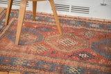 Antique Kazak rug section: distressed madder red field, tribal hooked guls, and faded blue motifs.