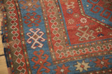 Distressed Kazak rug corner showcasing blue tribal hooked guls and red pawn design border.