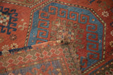 Distressed antique Kazak rug showing madder red field, blue guls, and reverse weave pattern.