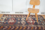 Distressed antique Shirvan rug with indigo field, red medallions, and vibrant rhythmic border.
