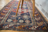 Distressed antique Shirvan rug showing worn texture, geometric motifs, and vivid color accents.