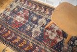Decorative distress on an antique Shirvan rug, highlighting indigo, red, and ivory geometric patterns.