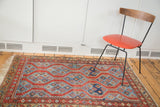 Antique Northwest Persian rug with geometric red field, indigo blue patterns, and textured fringe.