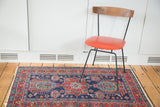 Distressed Heriz rug corner, showing star and meandering leaf borders in indigo and red.