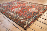 Distressed Baktiari rug with hexagonal panels, blossoming florals, and faded brick red.