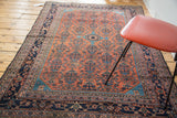 Distressed vintage Malayer rug corner showcasing decorative navy blue borders and brick red field.