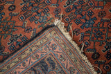 Distressed Malayer rug corner showing brick red herati field, blue borders, and worn fringe.