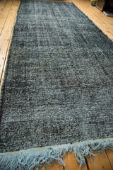 Distressed black and grey mottled texture of an overdyed rug, showing light blue fringe.