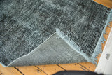 Corner of distressed overdyed vintage gallery runner, dark textured pile, foundation, and pale blue fringe.