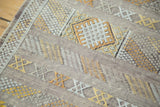 Moroccan Kilim rug with embroidered gold, ivory, and silver geometric patterns.