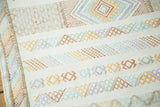 Embroidered geometric stripes in saffron, terra cotta, light blue, and mauve on a white kilim.