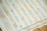Embroidered geometric guls, serpent motifs, and stripes in soft colors on a white kilim.