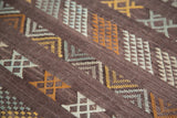 Detailed embroidery of gold, ivory, and blue geometric patterns on deep eggplant kilim.