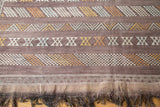 Eggplant kilim end with finely woven geometric patterns in ivory, gold, and silver, above dark fringe.