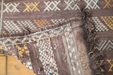 Embroidered details on a Moroccan Kilim rug, showing eggplant purple, ivory, and gold geometric patterns.