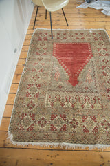 Corner of distressed Oushak Prayer rug with geometric cinnabar, sand, beige patterns, tattered fringe.