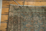 Distressed Malayer rug corner showing faded green, blush, charcoal herati design, secured fringe.