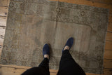 Distressed Oushak rug pile with muted bronze, blush colors and stepped mehrab details, shown with feet.