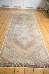 Distressed Oushak end, faded purple, tangerine, green geometric patterns, and fringe.