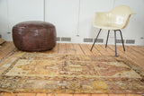 Distressed Oushak rug featuring an ornate medallion and muted saffron, mauve, and beige hues.