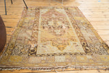 Frayed fringe and prominent holes on a distressed Oushak rug in muted gold.