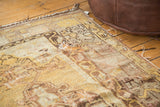 Distressed corner of vintage Oushak rug, featuring a large hole, saffron and beige tones.