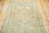 Angled view of a vintage Oushak runner, featuring faded sand and sea foam geometric starbursts.