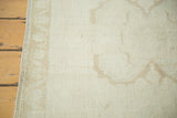 Secured side and hand-knotted texture of a vintage Oushak runner with faded bronze motifs.