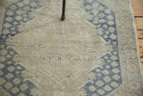 Distressed vintage Oushak pile with dusty blue floral motif on neutral sand.