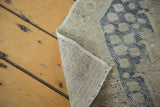 Folded vintage Oushak rug, revealing hand-knotted texture and distressed dusty blue, sand pattern.