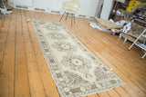 Distressed Oushak runner with beige field, brown scalloped medallions, and meandering border.