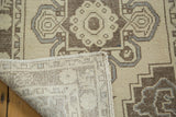 Folded corner of distressed Oushak rug revealing hand knotted back, beige field, and brown with silver patterns.
