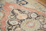 Distressed vintage Oushak rug: charcoal scalloped medallion, faded cinnabar field, floral patterns.