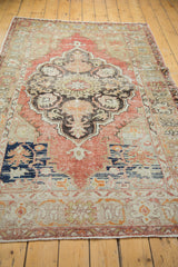 Corner of distressed Oushak rug showing faded cinnabar red, dark medallion detail, navy, and sand.